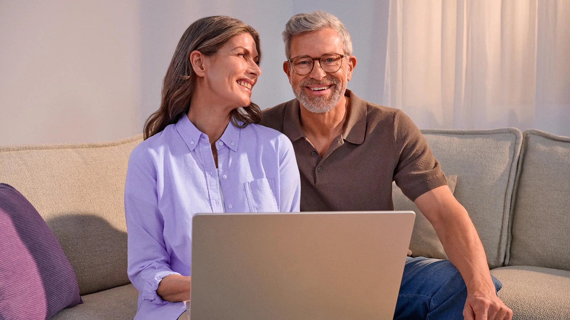 Casal feliz a usar tecnologia, ambos a usar aparelhos auditivos.