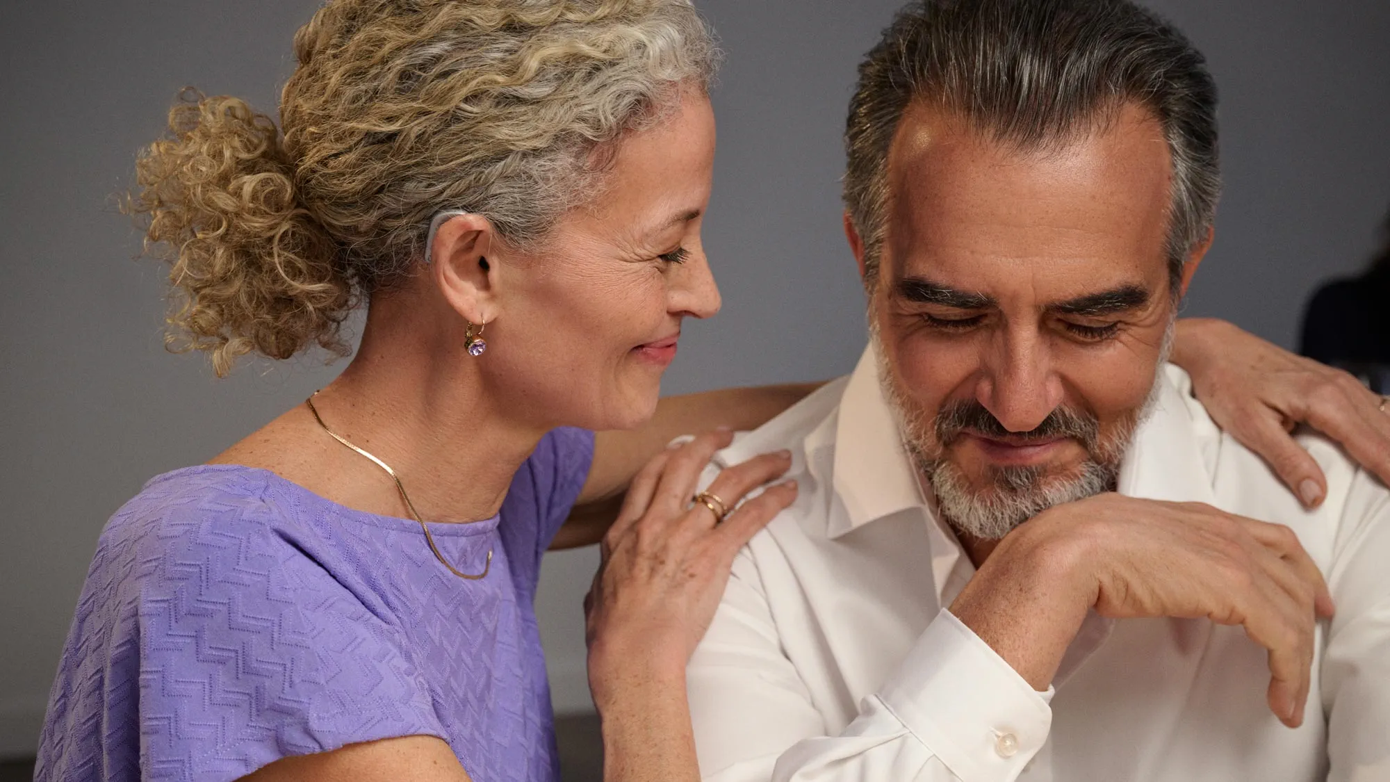 Casal a sorrir orgulhosamente, mostrado de perto com os aparelhos auditivos visíveis.