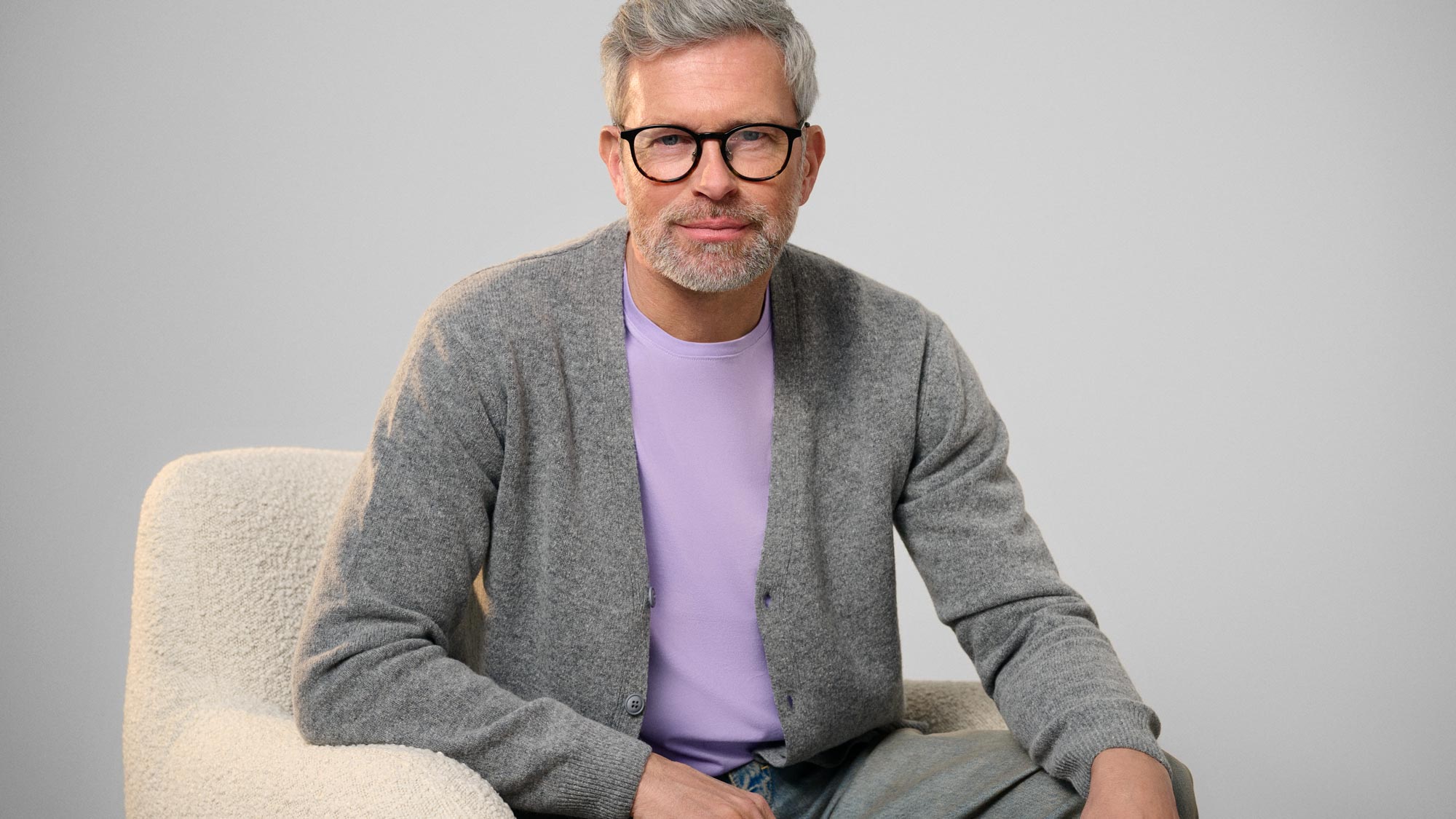 Man wearing glasses, sitting and reflecting on hearing loss.