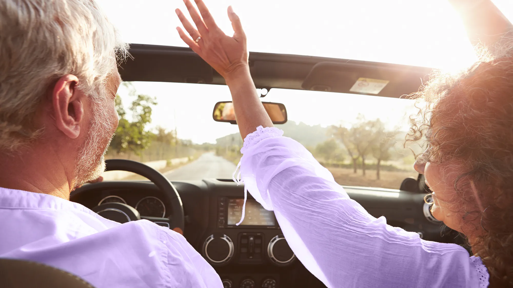 Couple driving in car on a sunny day, both wearing hearing aids