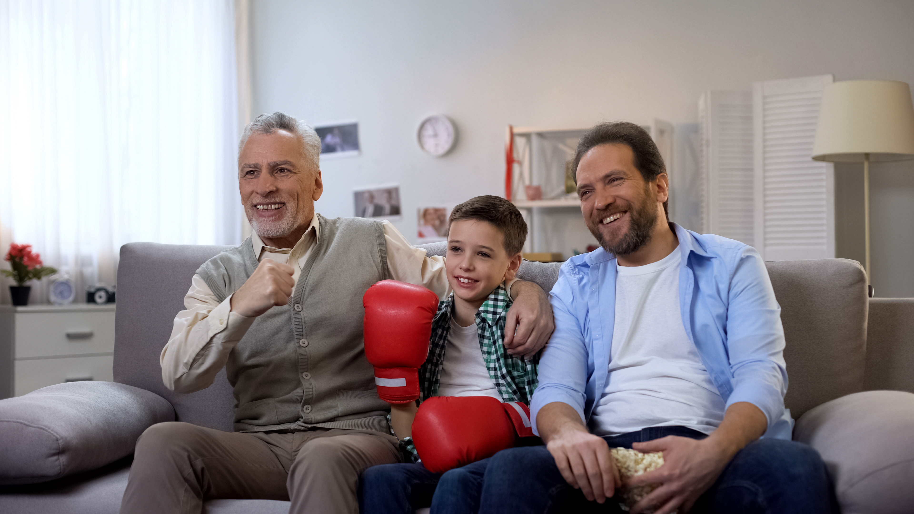Smiling male family members watching boxing on tv, cheering for favorite boxer wearing hearing aids