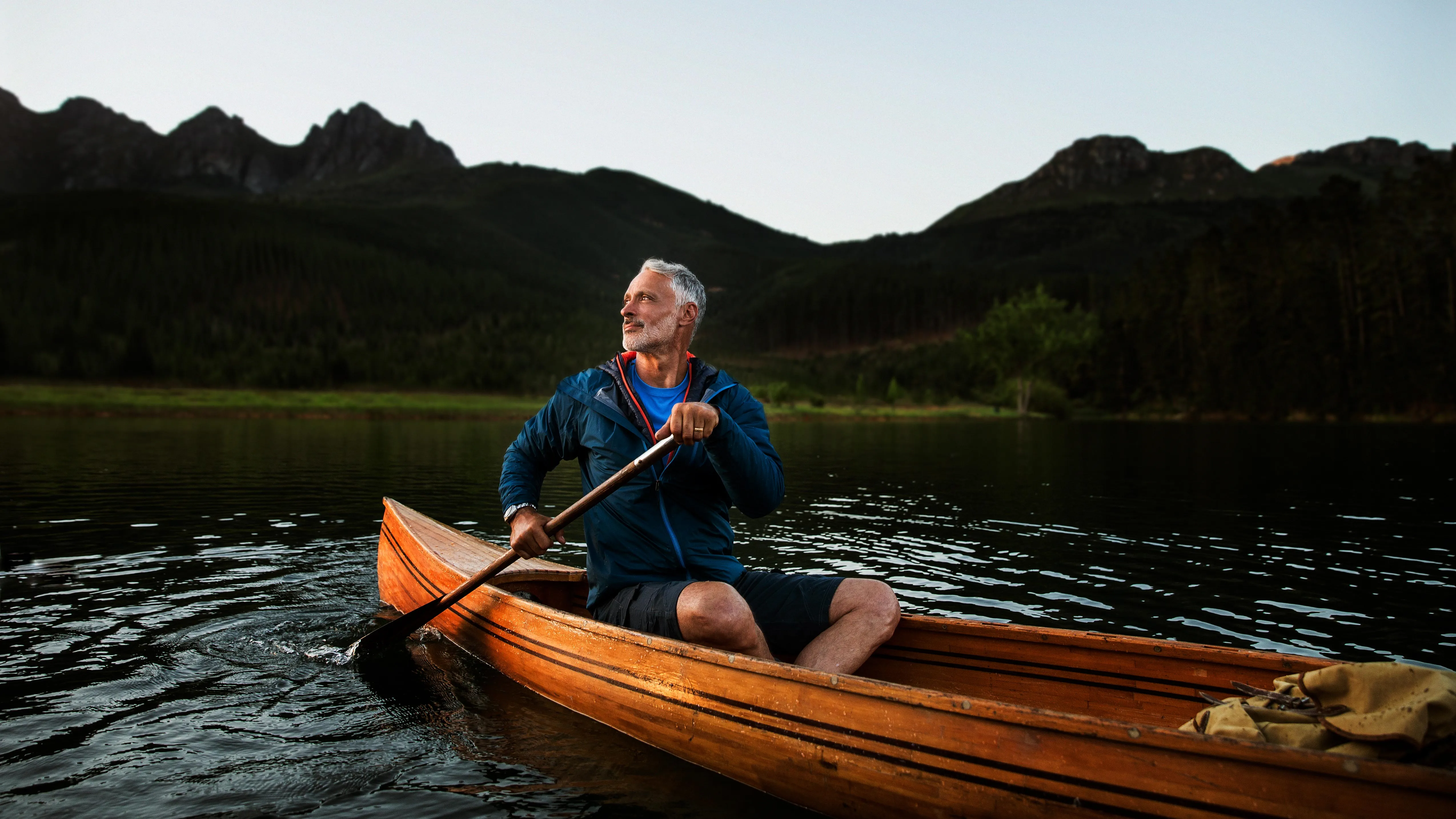 A middle-aged man canoeing on a river while wearing hearing aids, enjoying the outdoors and better hearing.