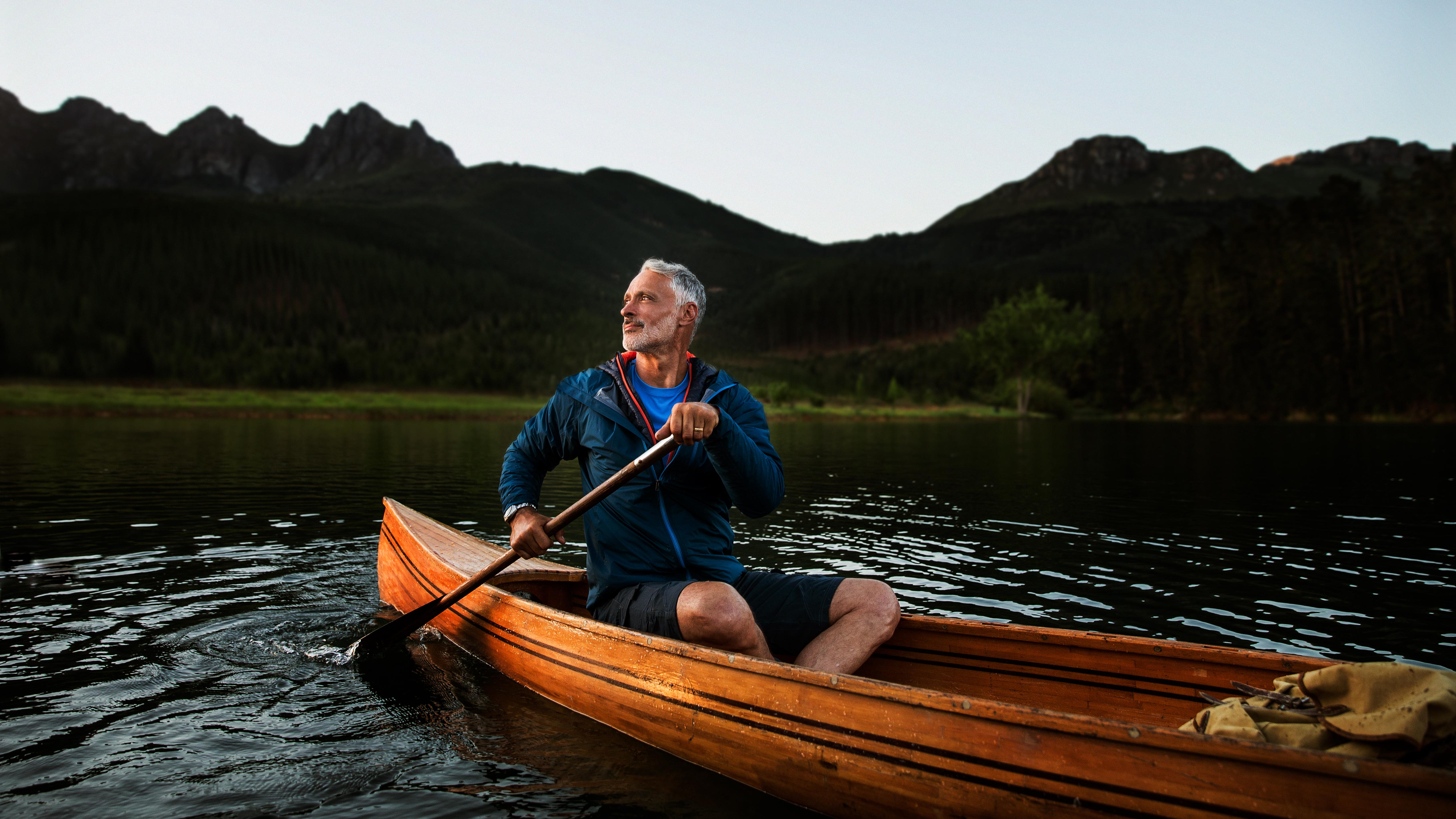 A middle-aged man canoeing on a river while wearing hearing aids, enjoying the outdoors and better hearing.