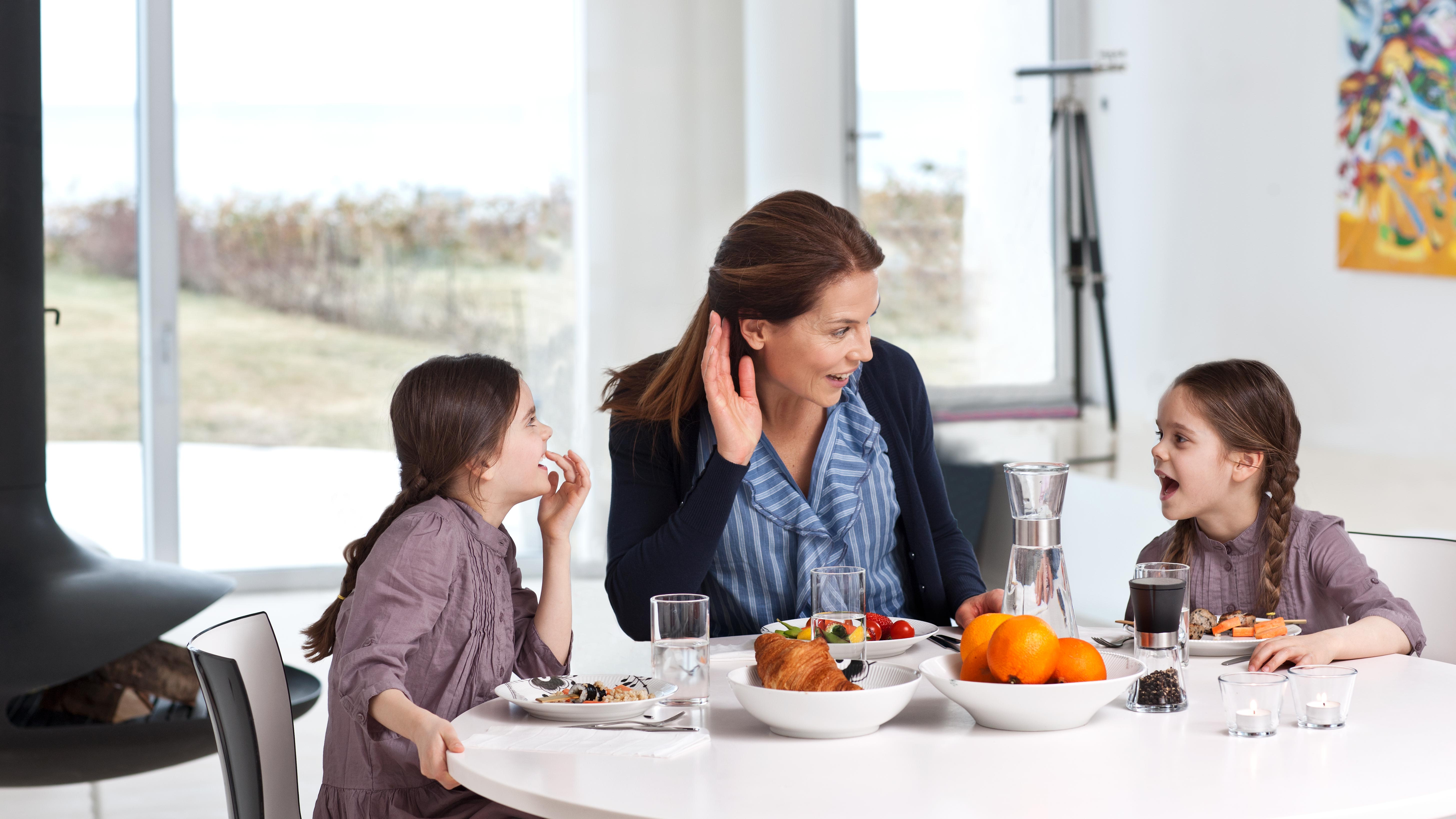 A mother wearing hearing aids with her two daughters eating breakfast and enjoying quality time together.