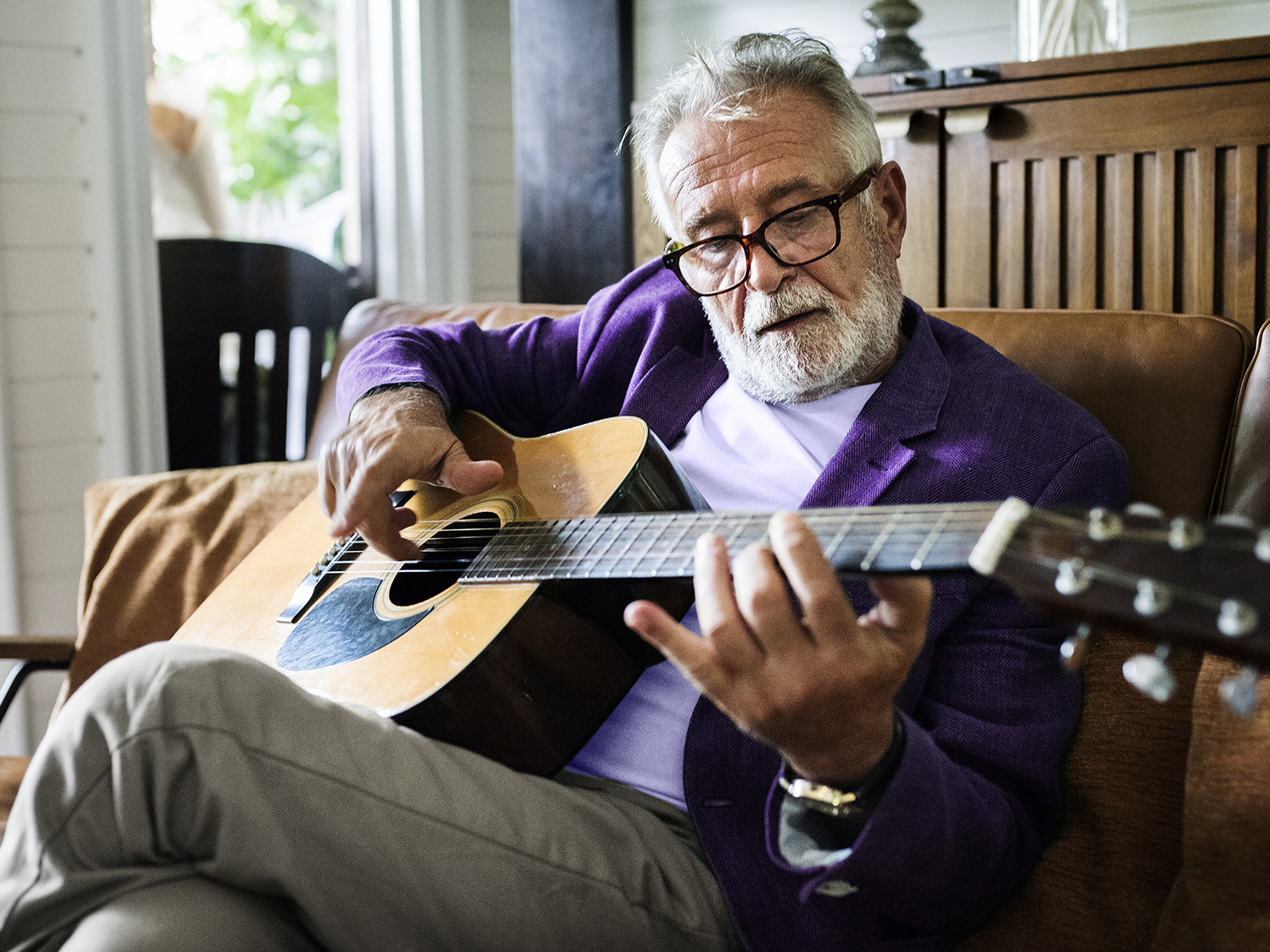 An elderly man playing an acoustic guitar while wearing hearing aids