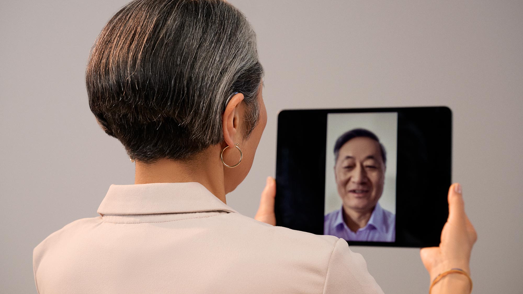 A woman wearing Signia Pure hearing aids, participating in a Teams meeting on a tablet.