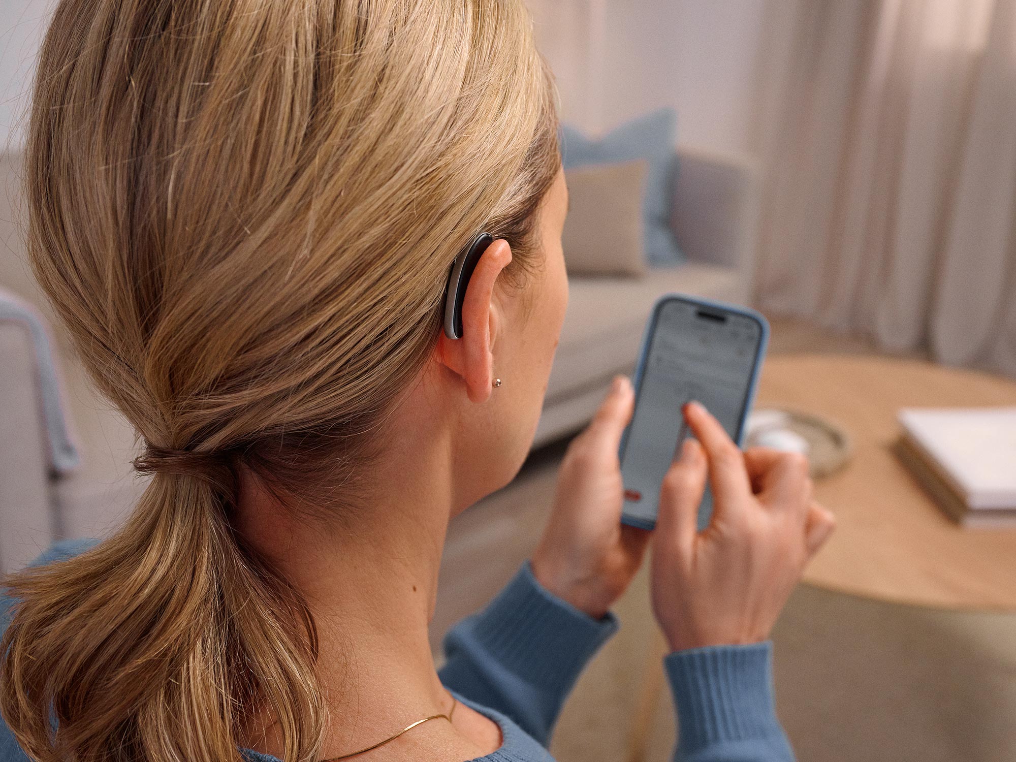 Woman on the phone wearing Signia Styletto hearing aids controling hearing aids on phone