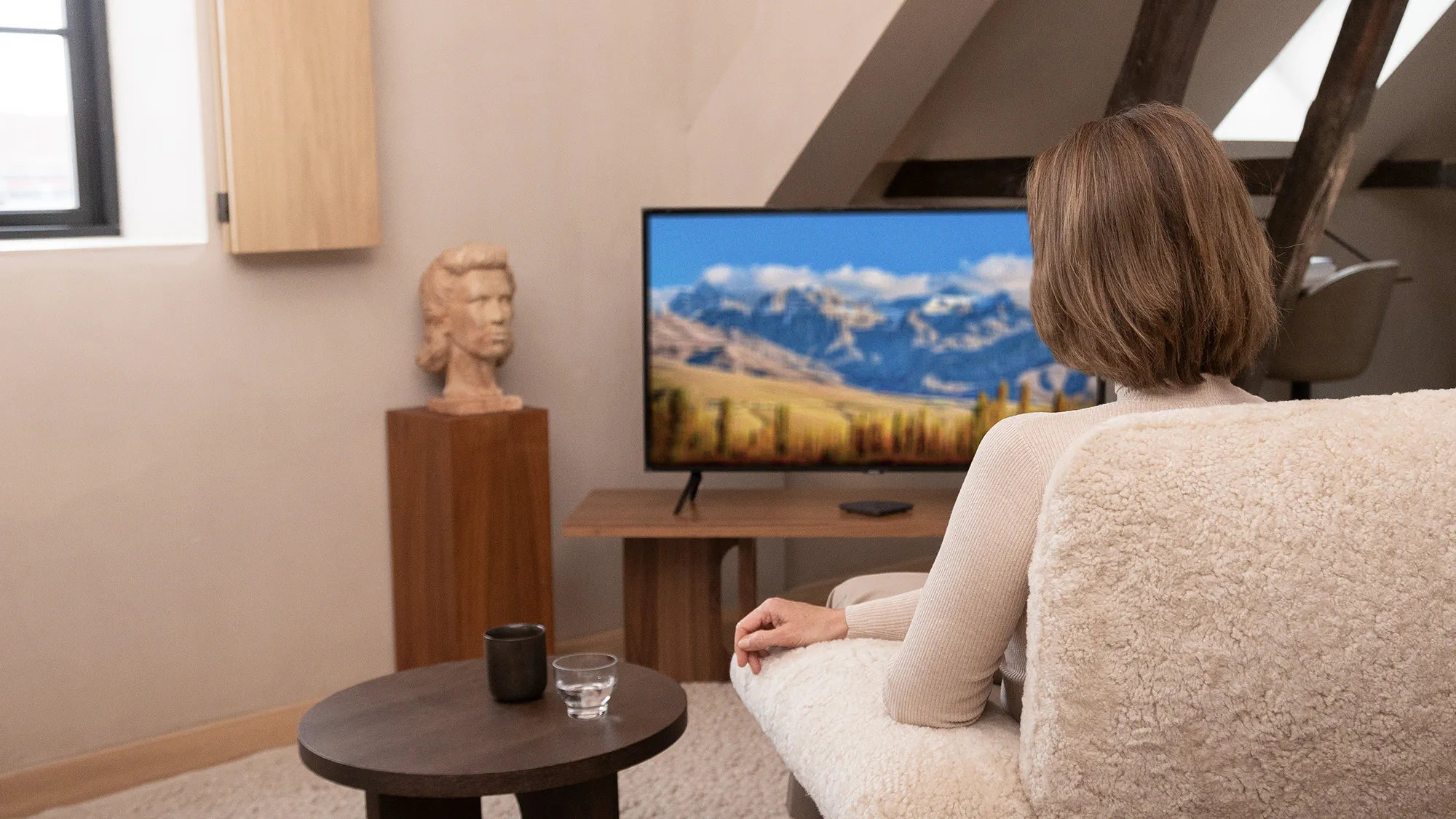 The woman is wearing Widex Moment Sheer hearing aids and is receiving the sound directly streamed to her Widex TV Play.