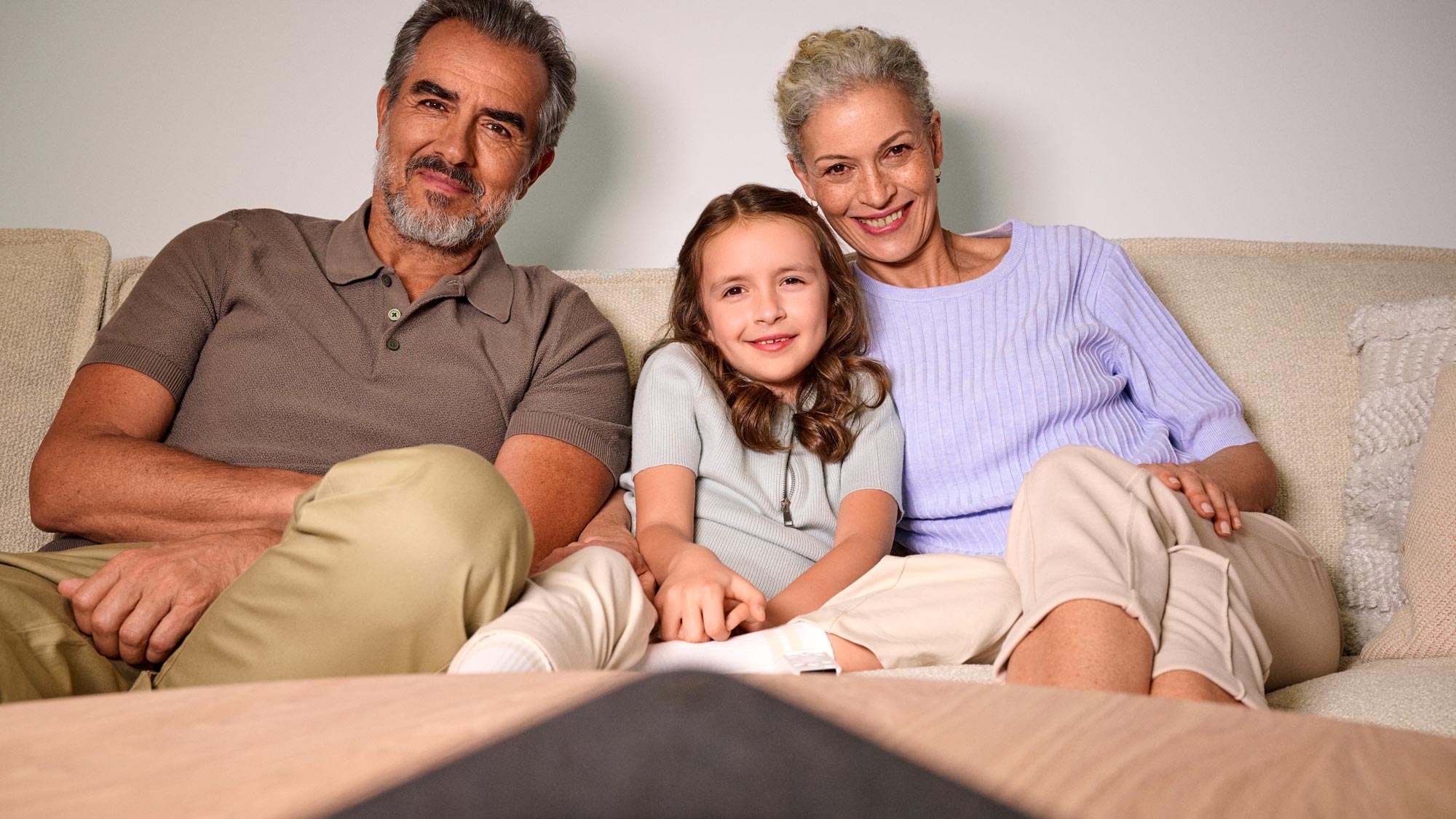 A family is at home on the sofa, with one member wearing hearing aids
