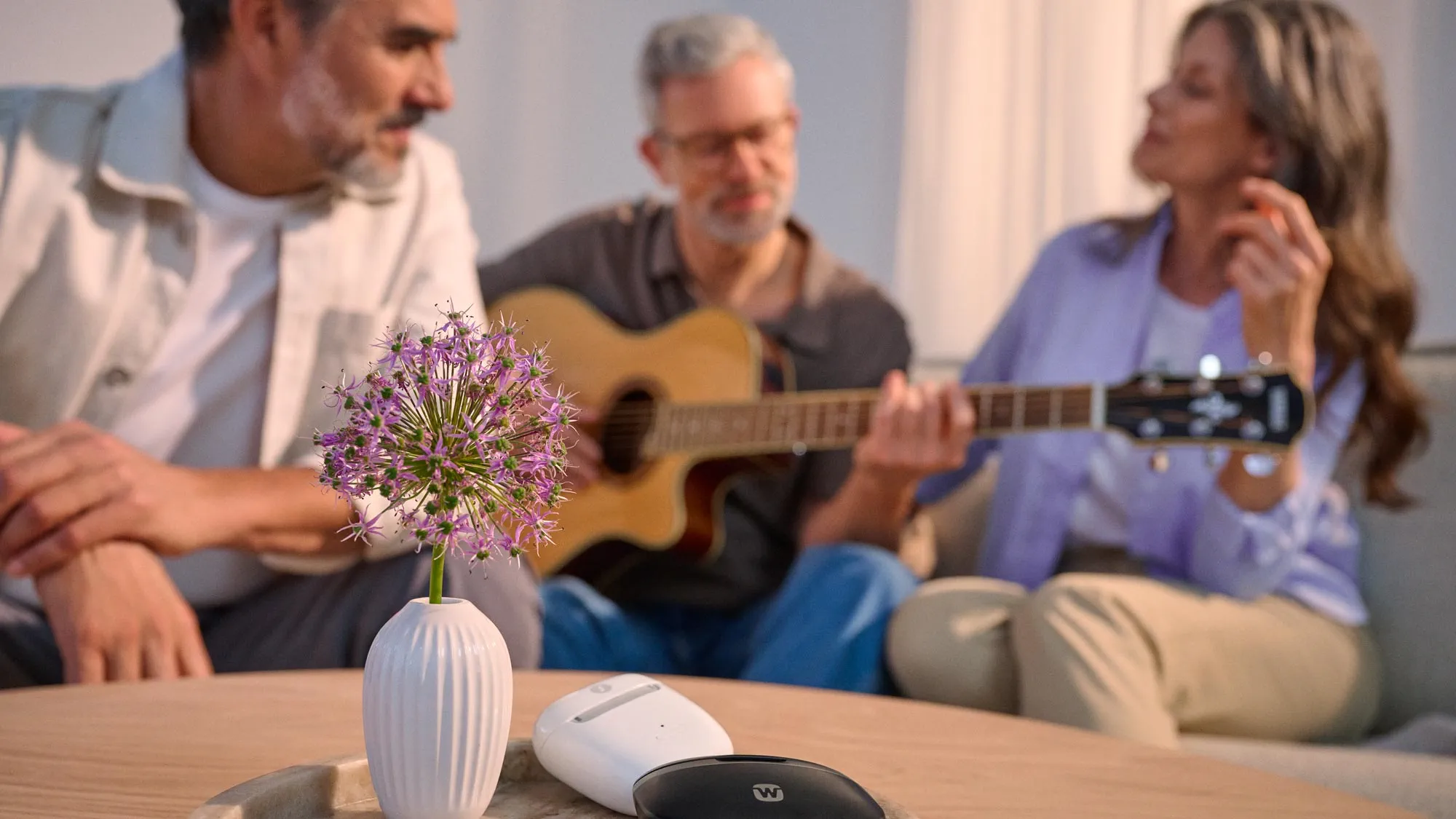 Friends making music on a couch, with hearing aid chargers nearby