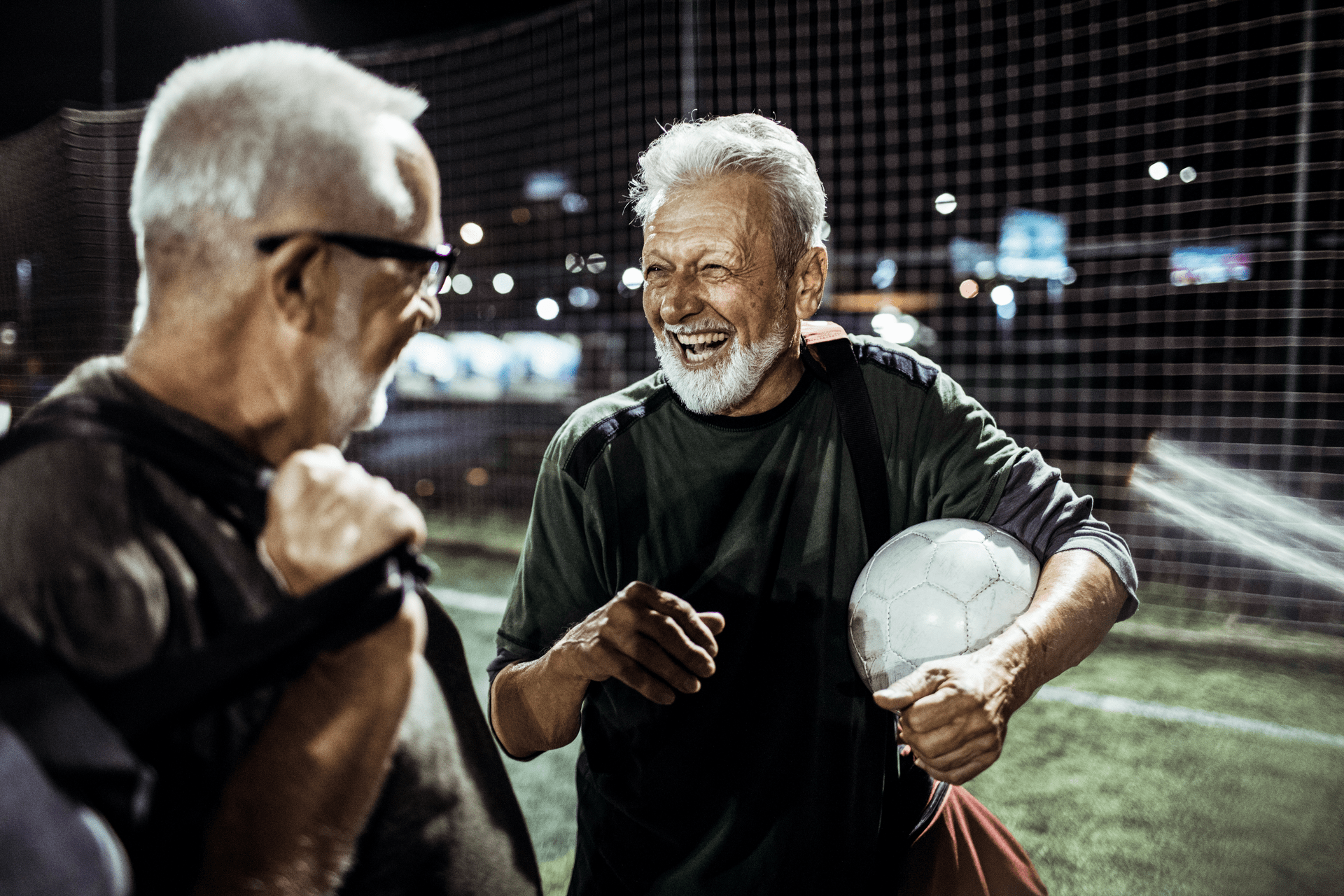 Two senior men laughing together after a soccer game at night