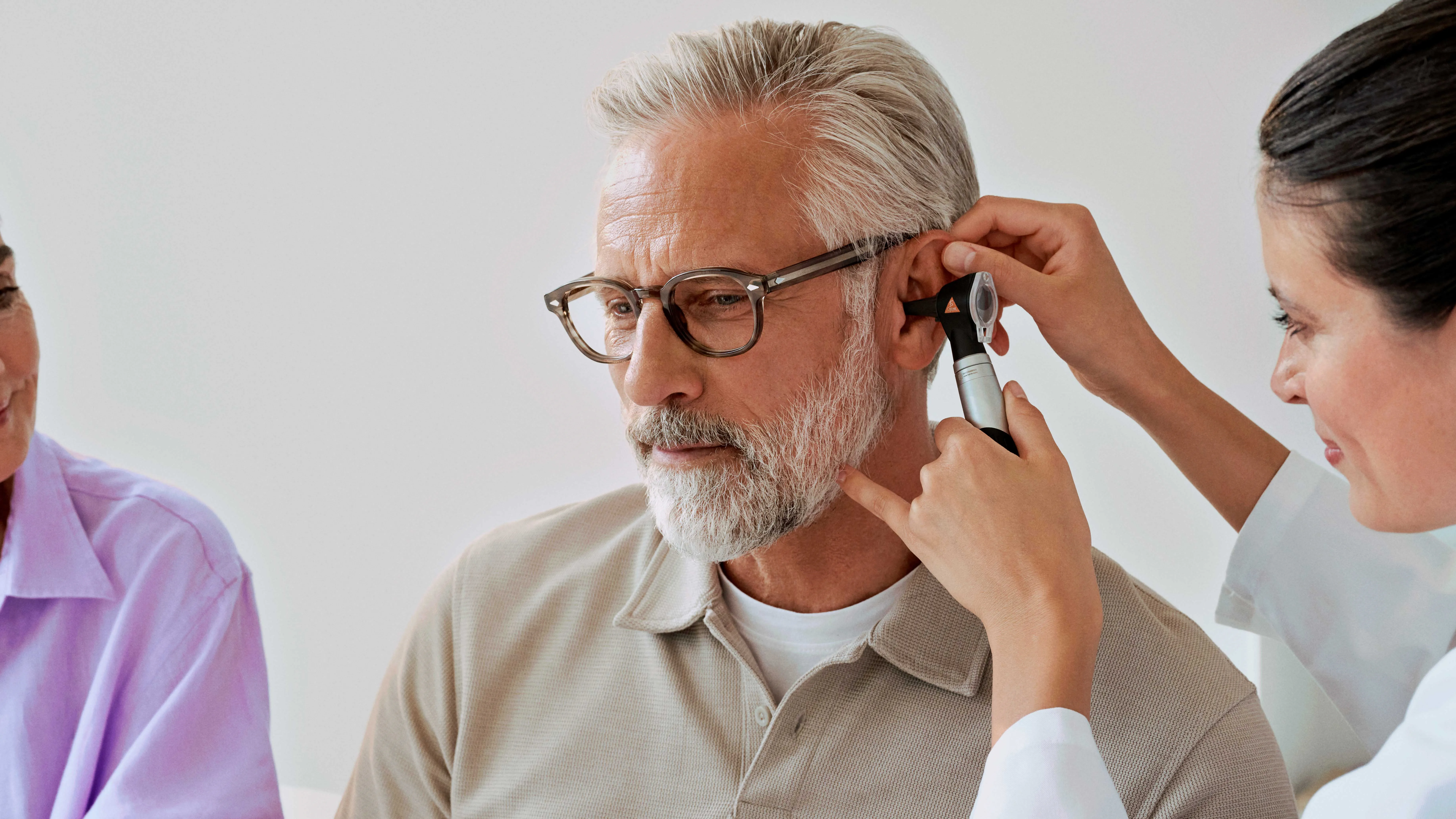 An audiologist performing an otoscopy on a man, checking his hearing health.