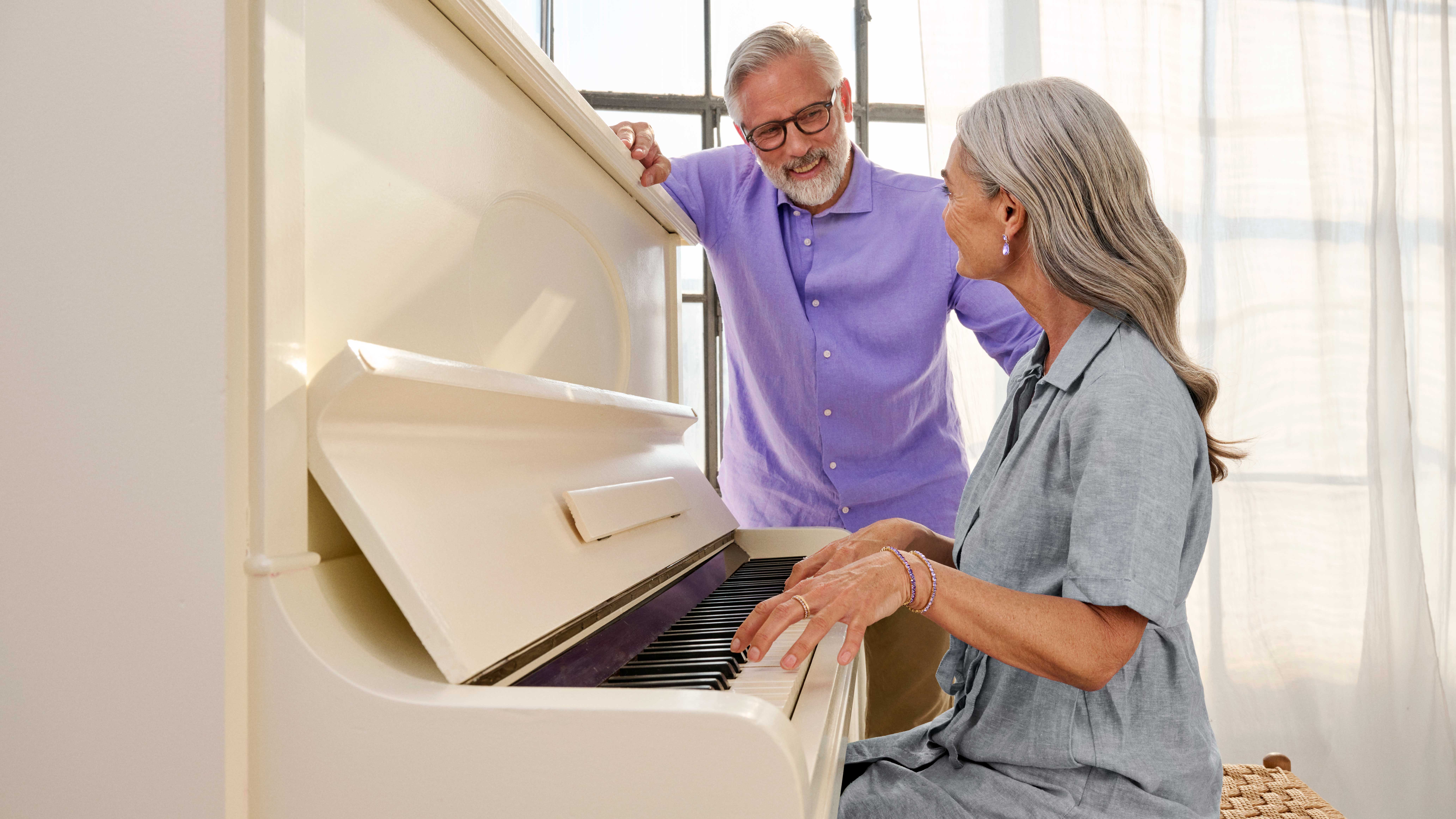 A couple seated at a piano, sharing a musical moment with hearing aids.
