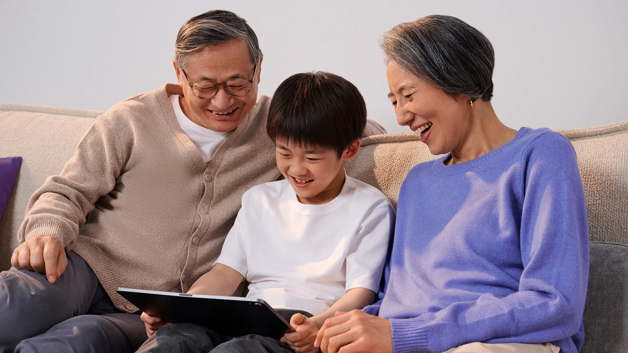 Family relaxing on a couch while using a tablet, with hearing aids enhancing the experience.