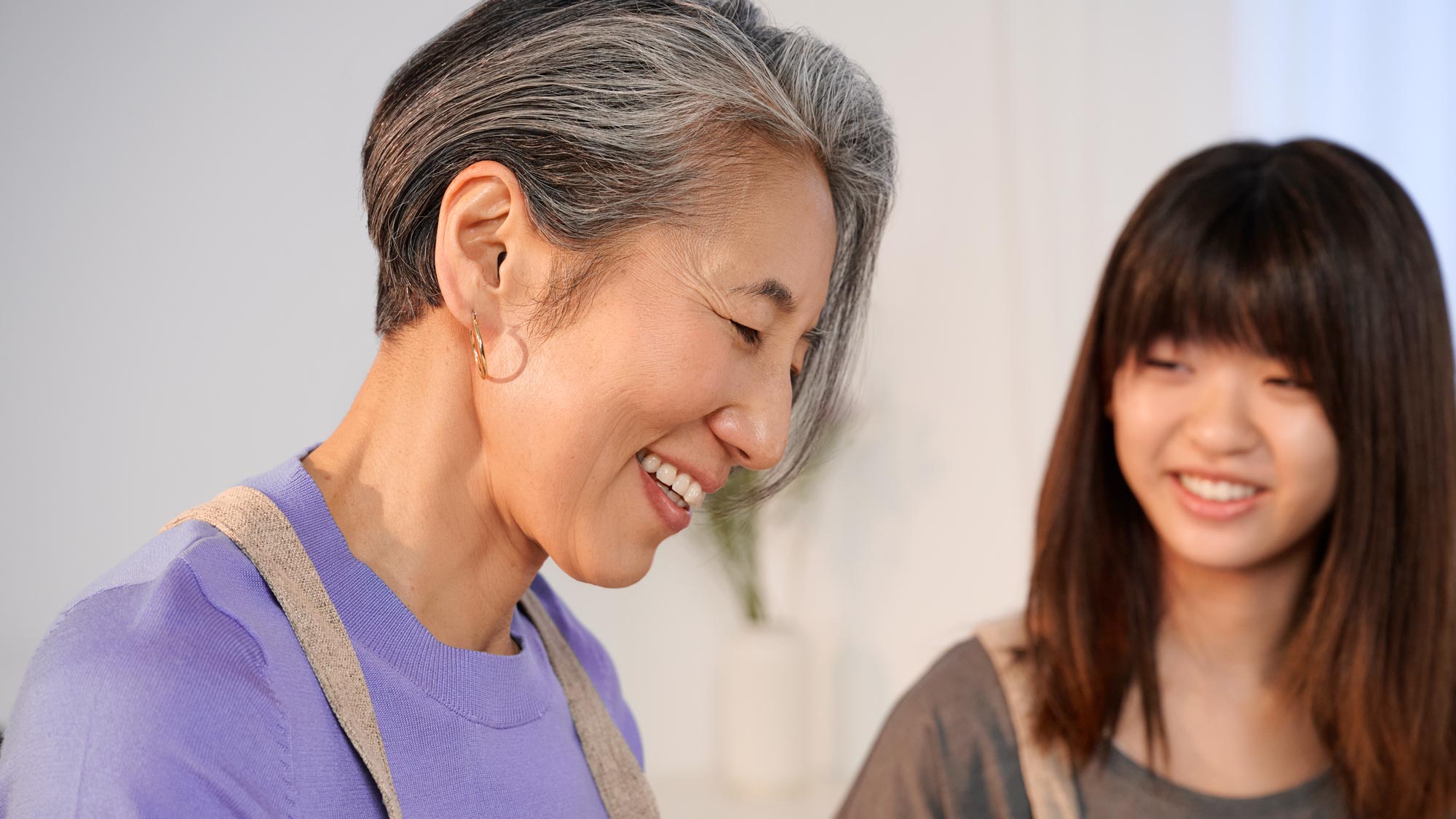 A grandmother smiling as she cooks in a kitchen, wearing her hearing aids