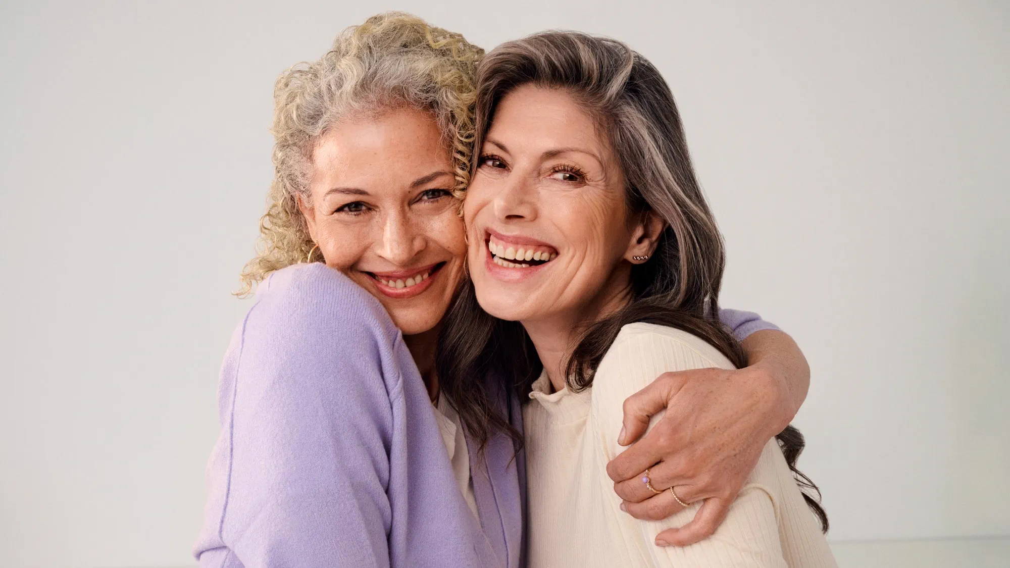 Women friends hugging warmly, with their hearing aids visible.