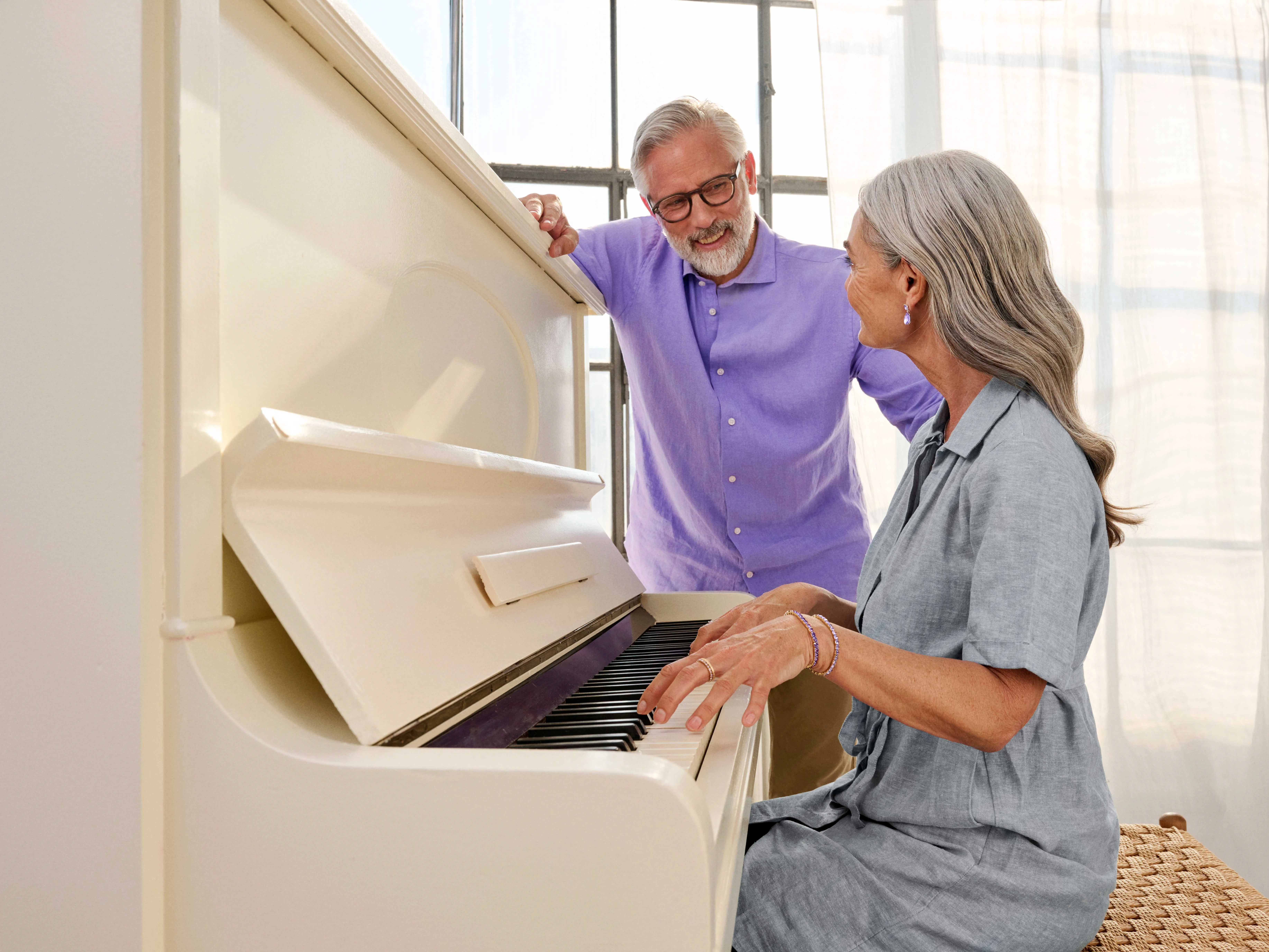 A couple seated at a piano, sharing a musical moment with hearing aids.