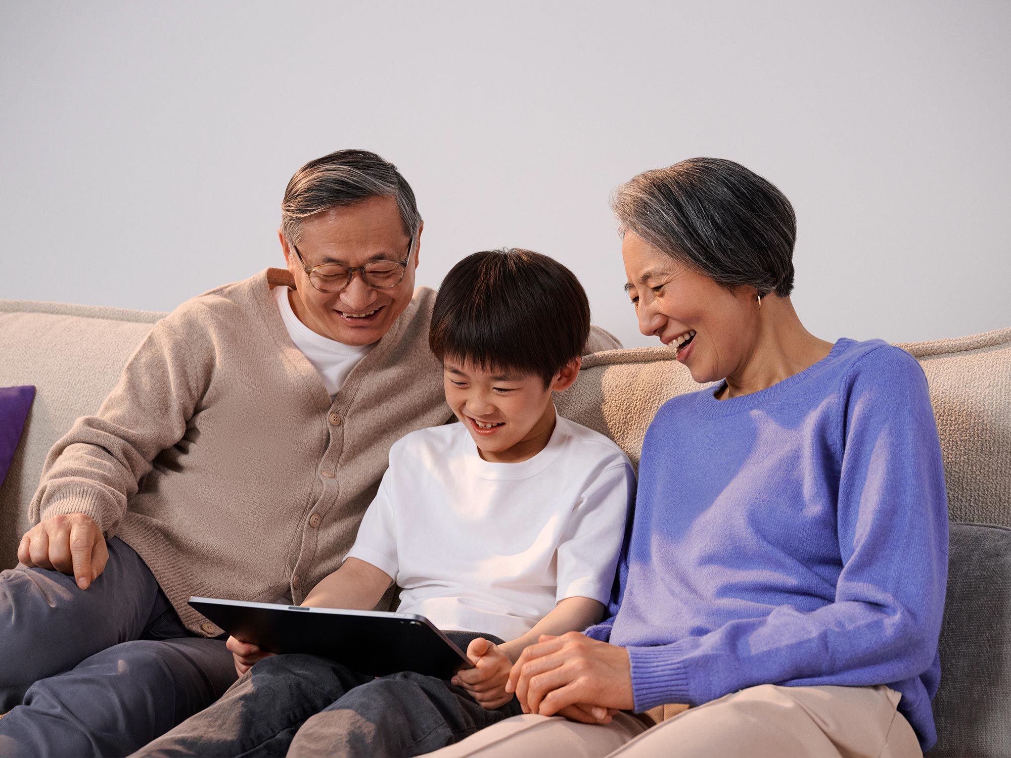 Family relaxing on a couch while using a tablet, with hearing aids enhancing the experience.
