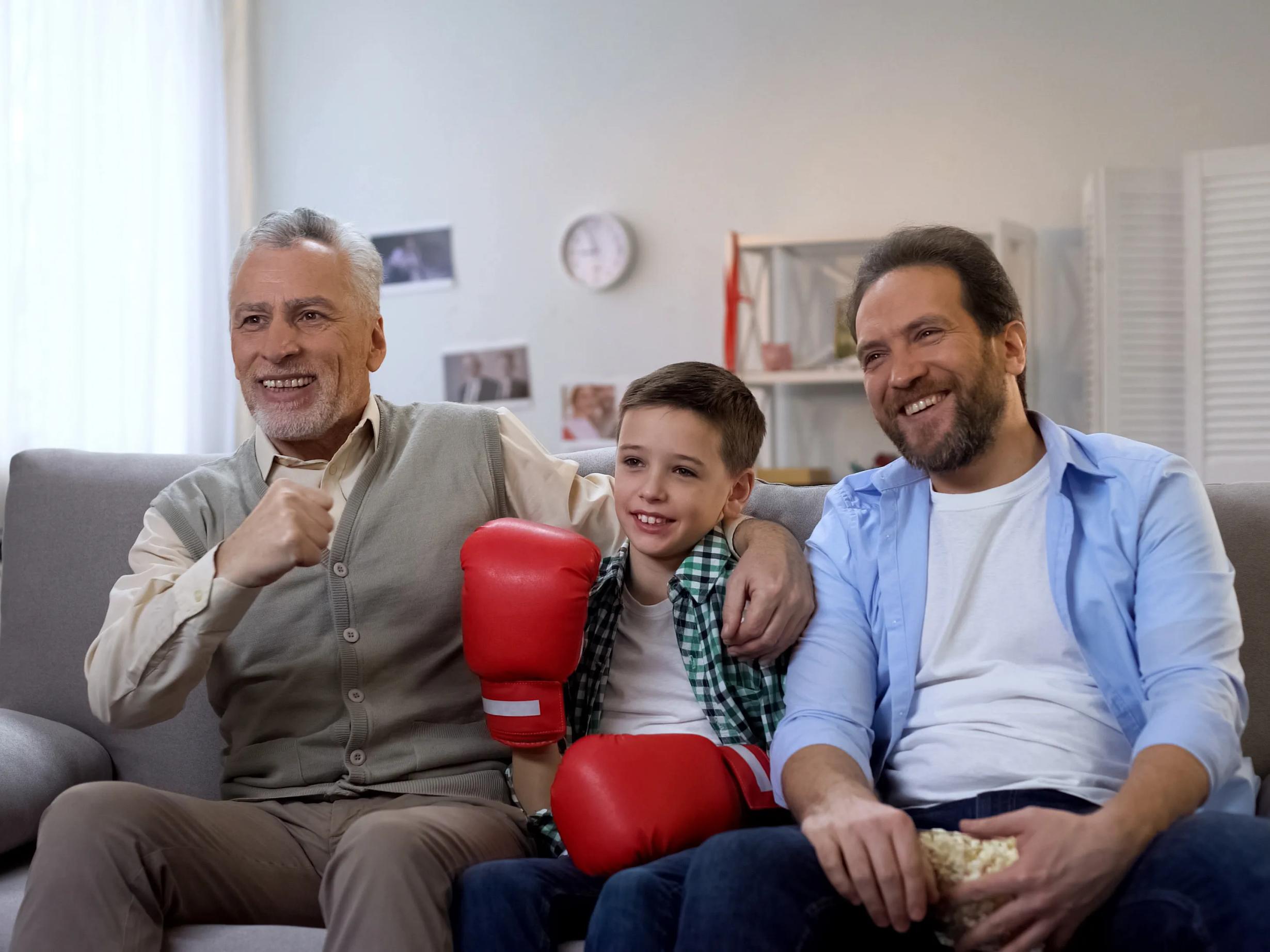 Smiling male family members watching boxing on tv, cheering for favorite boxer wearing hearing aids